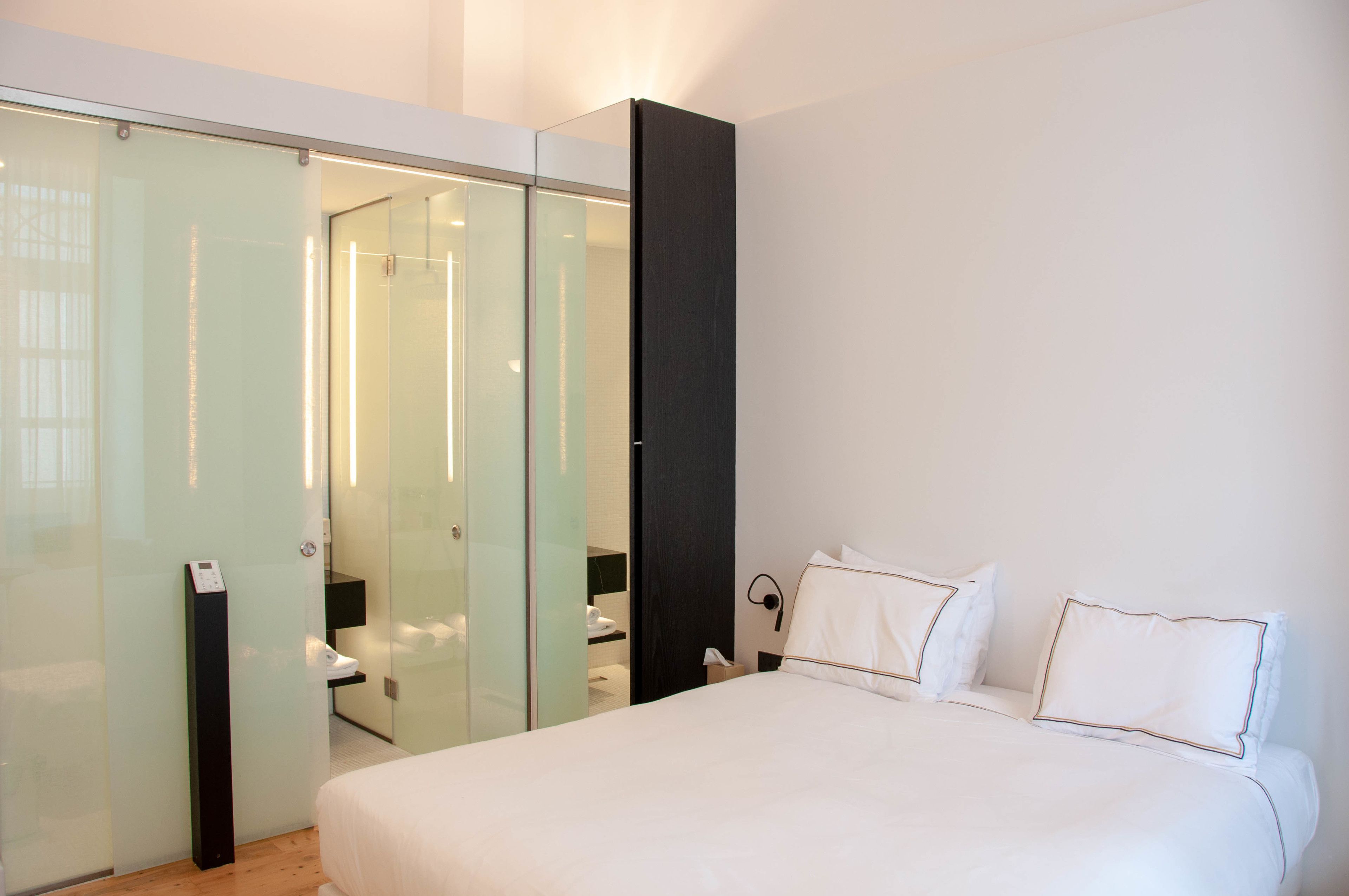 Et moderne hotelværelse med en stor seng, et glasafskærmet walk-in closet og et separat badeværelsesområde.