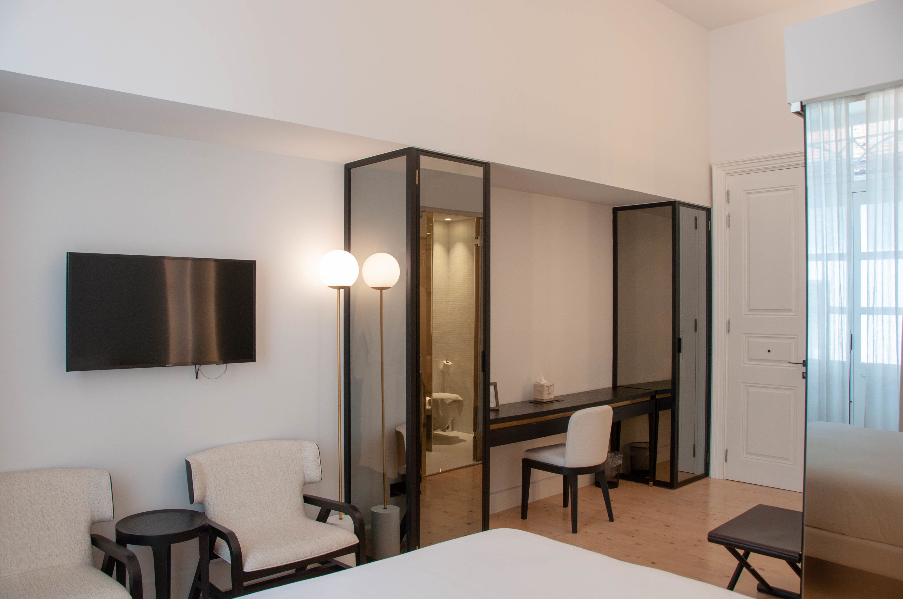 Une chambre d’hôtel comprenant un lit, un bureau, deux chaises, une télévision et un miroir.