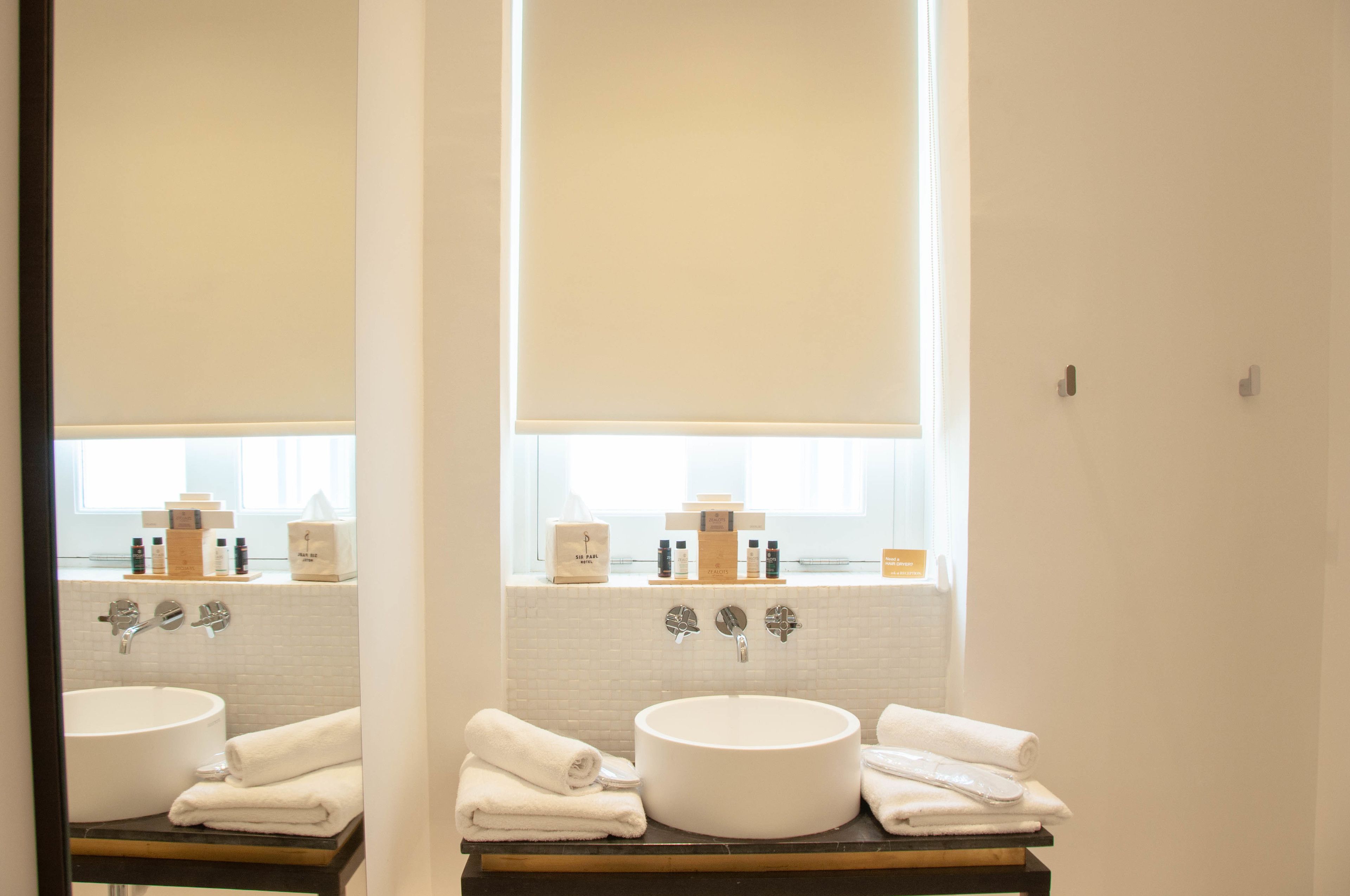 Un baño con un lavabo redondo, dos grifos y una ventana sobre el lavabo. Hay toallas apiladas en la encimera y artículos de tocador en el alféizar de la ventana.