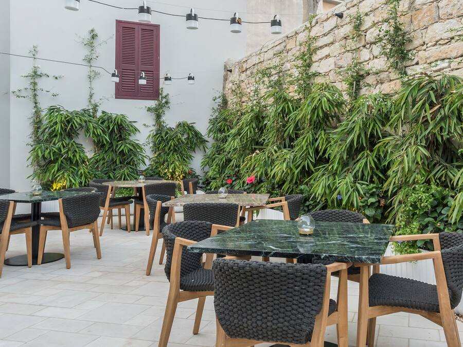 An outdoor seating area with tables and chairs, surrounded by lush greenery and a stone wall.