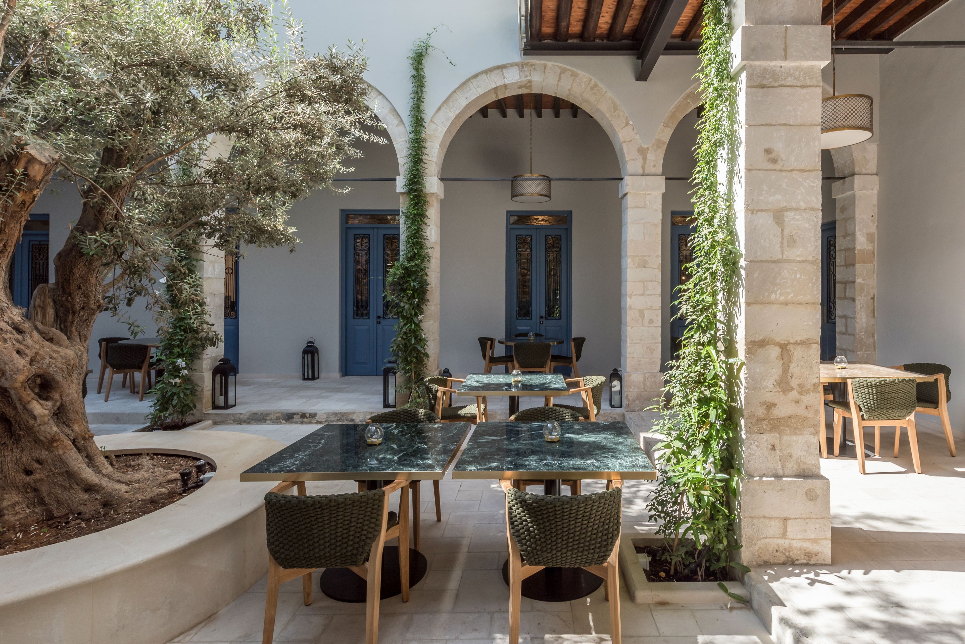 An outdoor dining area with stone arches, wooden tables, and chairs.