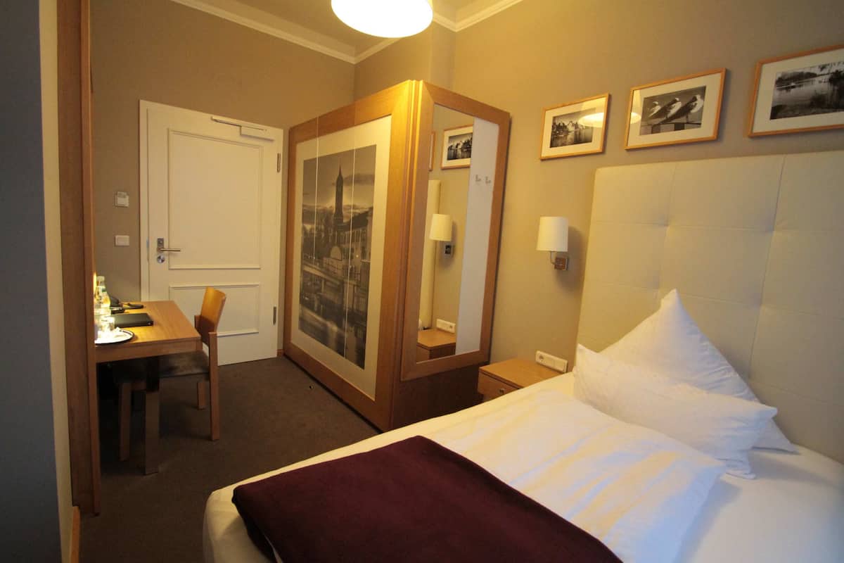 Une chambre d’hôtel comprenant un lit, un bureau, une chaise, une armoire et un miroir.