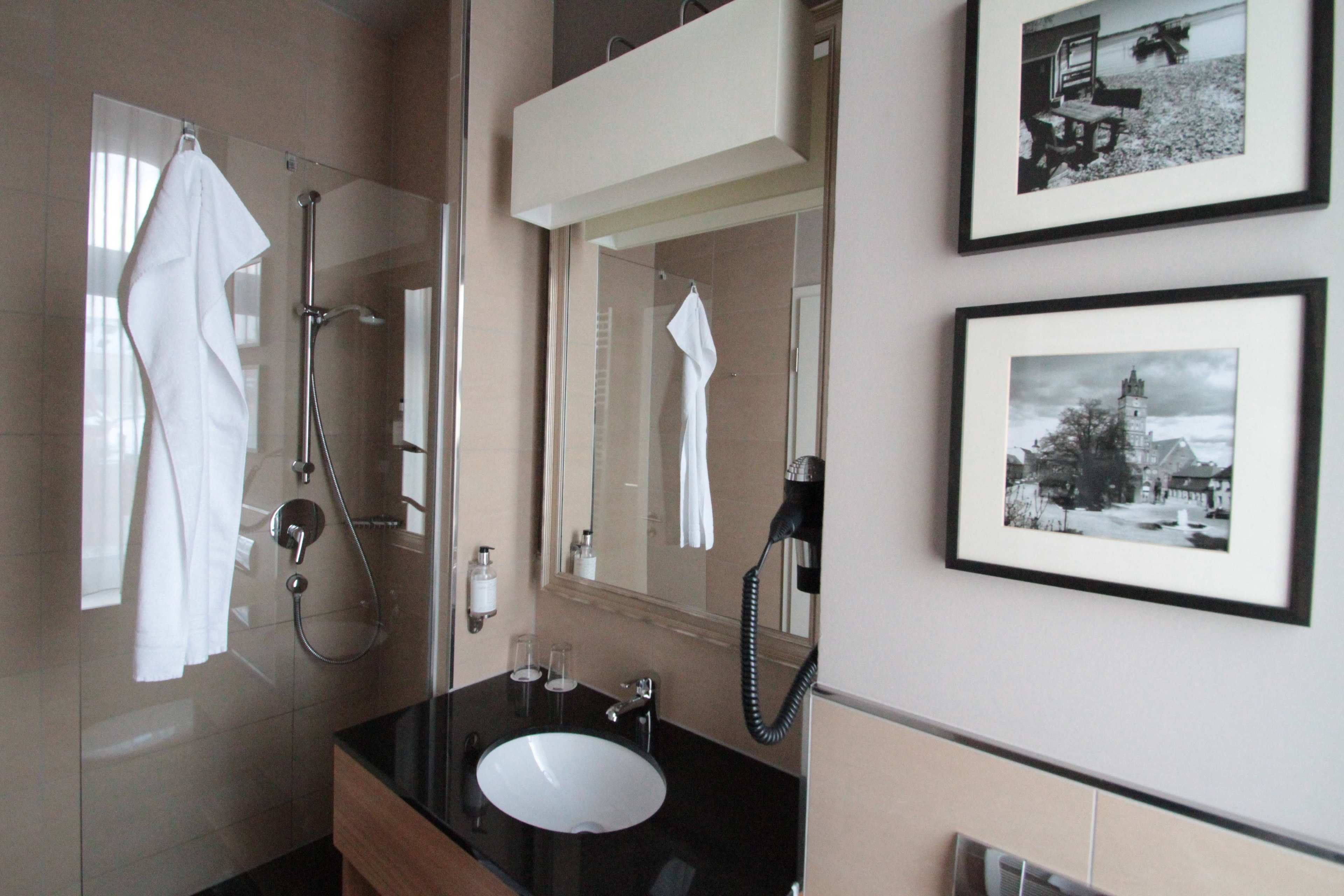 Een badkamer met een wastafel, spiegel, handdoekhouder en douche.