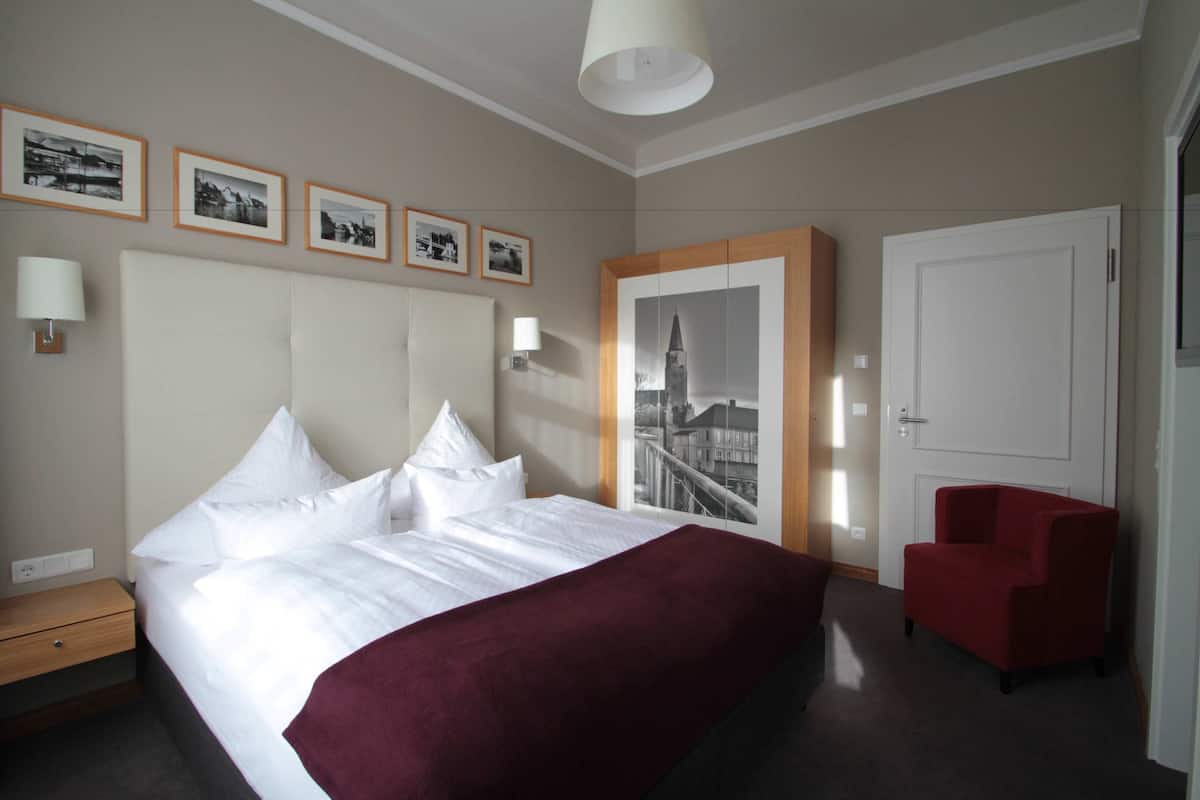 Une chambre d’hôtel avec un grand lit, un fauteuil rouge et des tableaux encadrés au mur.