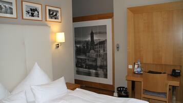 Quarto de hotel com cama, escrivaninha, cadeira, luminária, quadro emoldurado e garrafa de água.