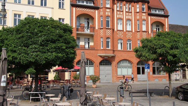 Un bâtiment à la façade en briques rouges, doté de nombreuses fenêtres et d’un balcon.