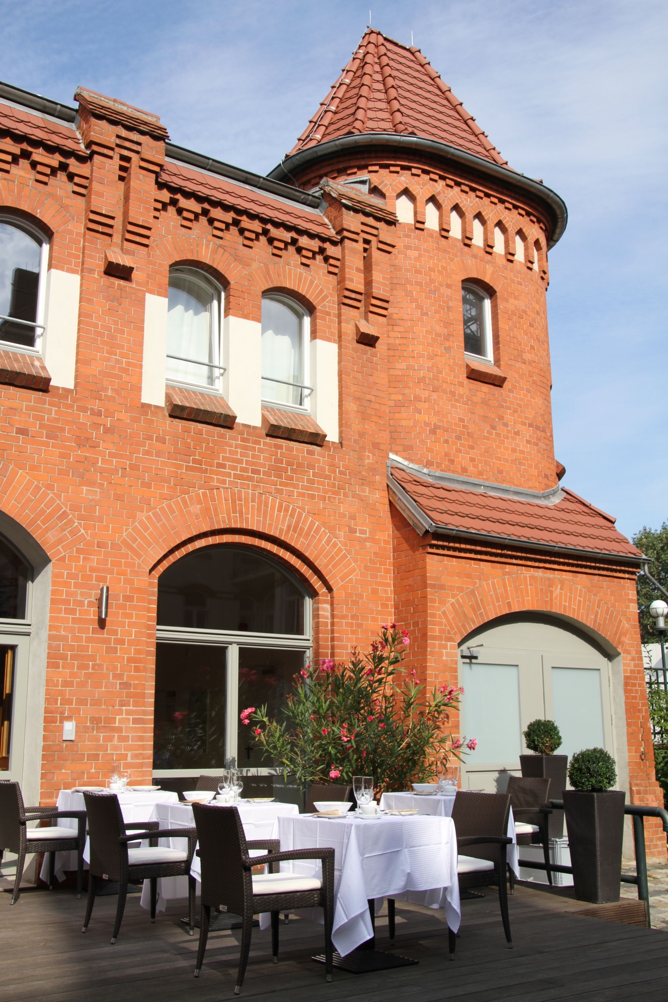 A brick building with a tower, outdoor dining area with tables and chairs, and a flower arrangement.