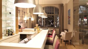 Un espace bar doté d’un long comptoir, de plusieurs suspensions décoratives et d’un coin salon avec des bancs rembourrés.