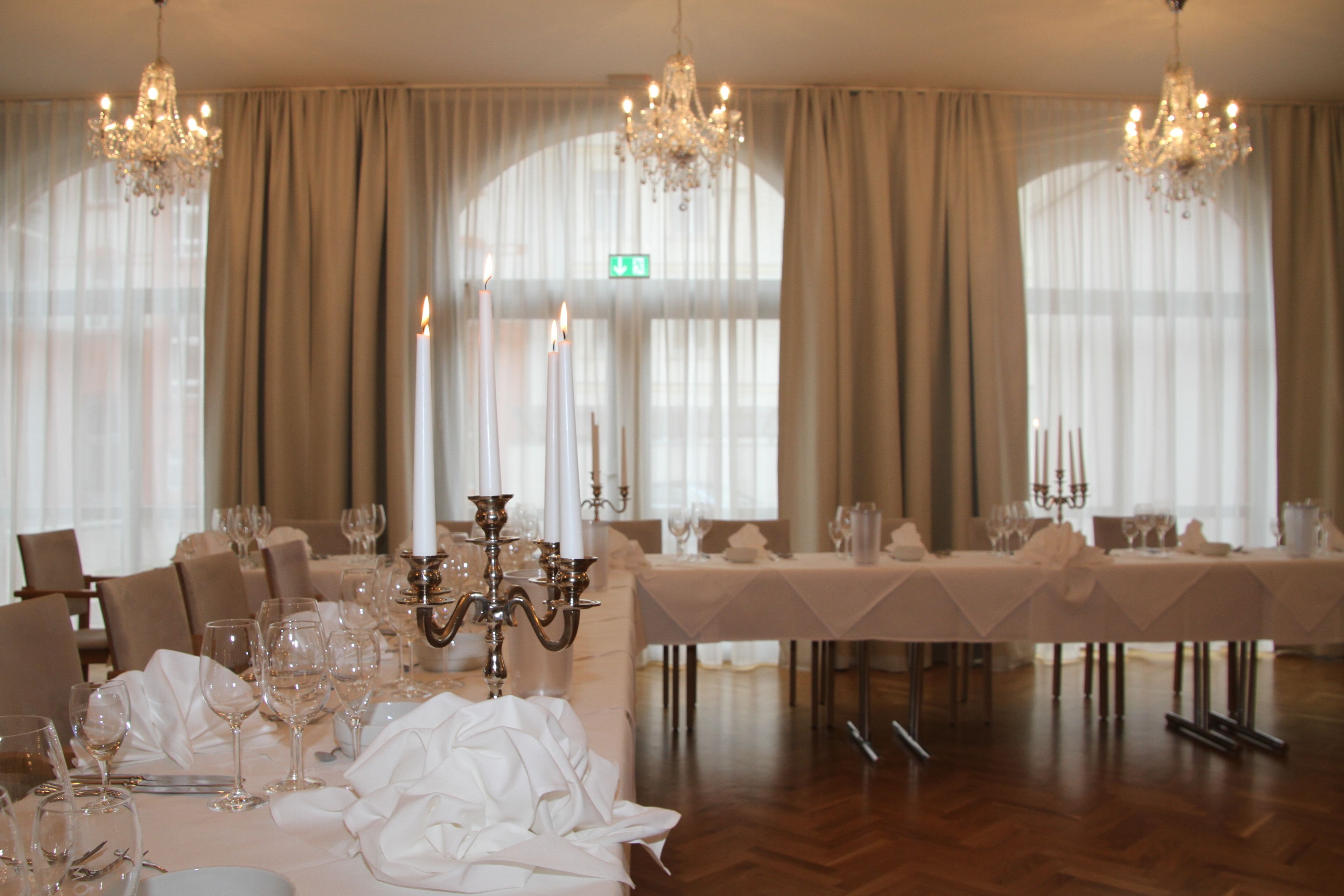 A formal dining room with a long table set for a meal, chandeliers, and large windows with curtains.