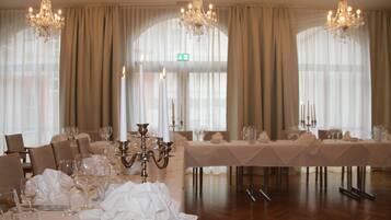 A formal dining room with a long table set for a meal, chandeliers, and large windows with curtains.