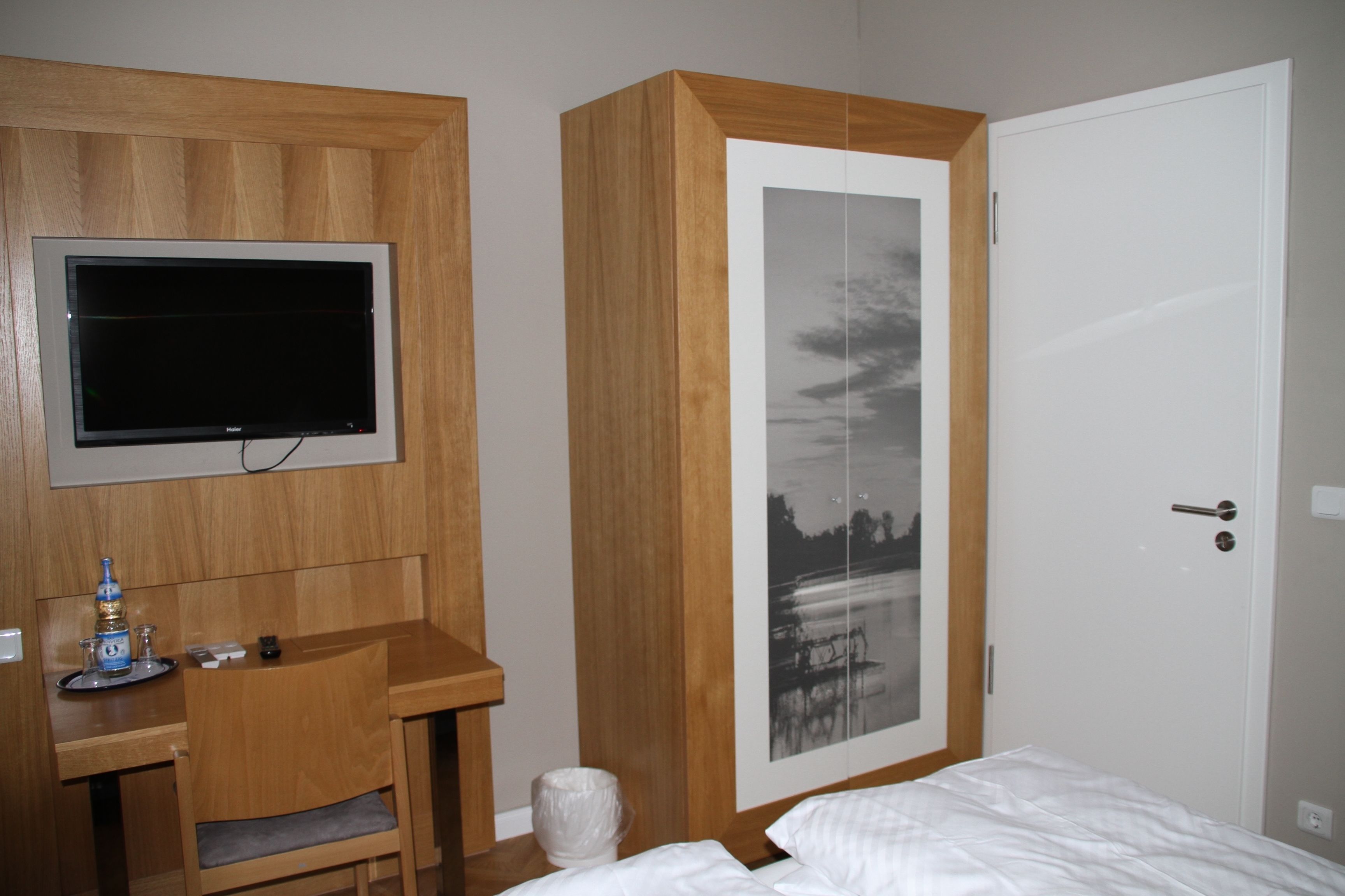 Un dormitorio con un escritorio de madera, un televisor, una cama y una puerta con una fotografía en blanco y negro.
