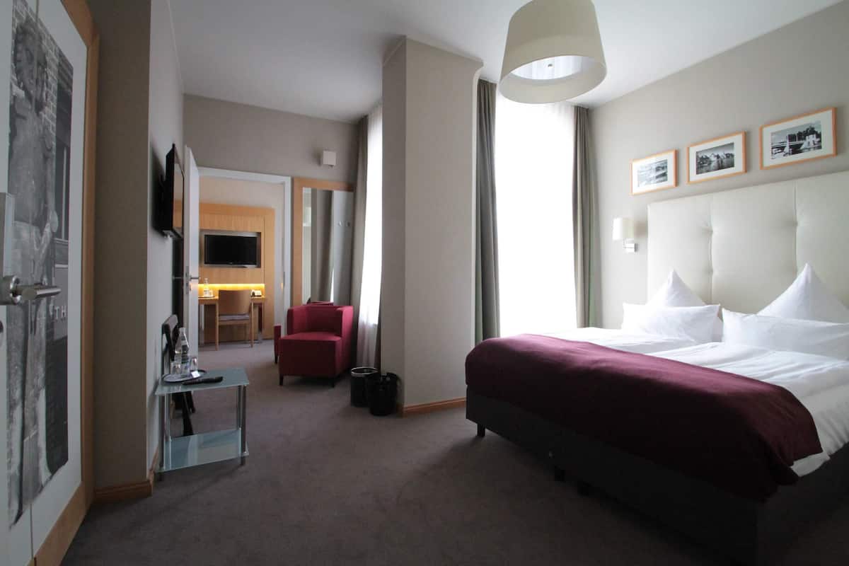 Une chambre d’hôtel avec un grand lit, un téléviseur fixé au mur, un bureau avec une chaise et un fauteuil rouge.