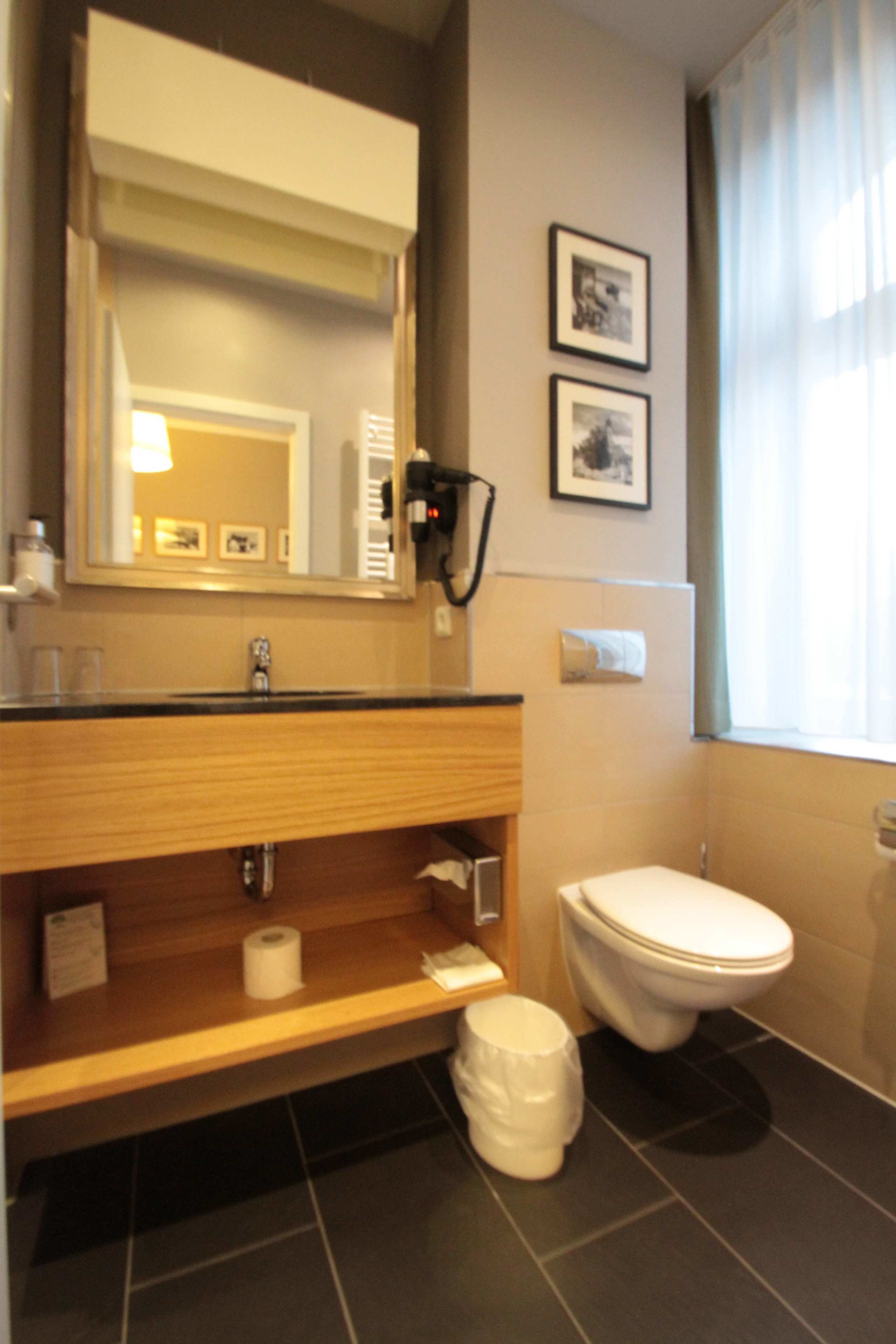 A bathroom with a wooden vanity, a toilet, a mirror, and two framed pictures on the wall.