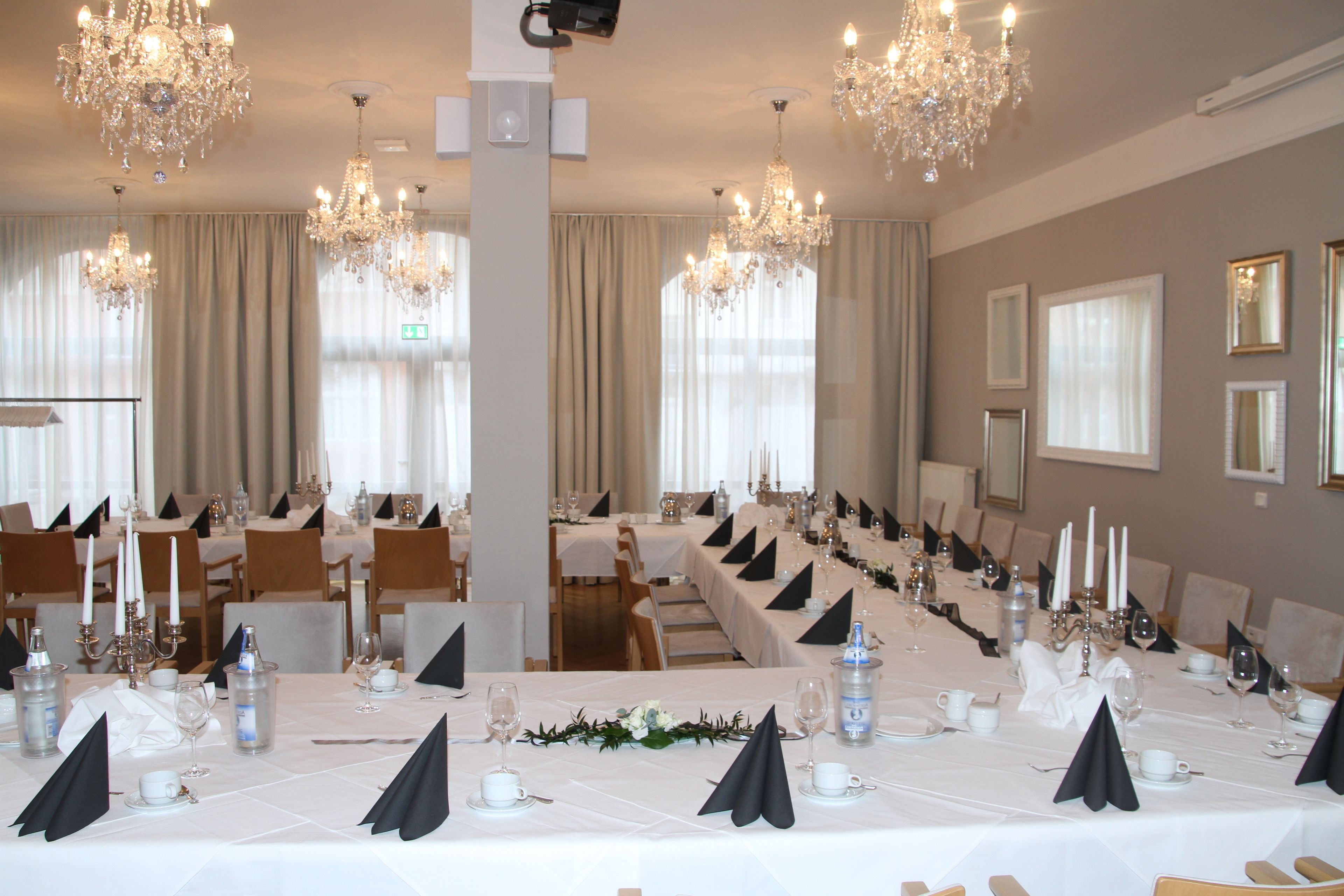 Un salón de banquetes con largas mesas dispuestas para un evento formal, decorado con candelabros de cristal y elegantes centros de mesa.