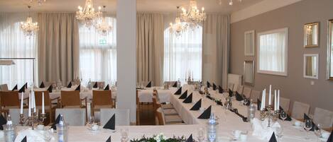 Un salón de banquetes con largas mesas dispuestas para un evento formal, decorado con candelabros de cristal y elegantes centros de mesa.