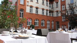 Une cour avec des tables dressées pour le repas, entourée d’un bâtiment en briques doté de nombreuses fenêtres et de balcons.