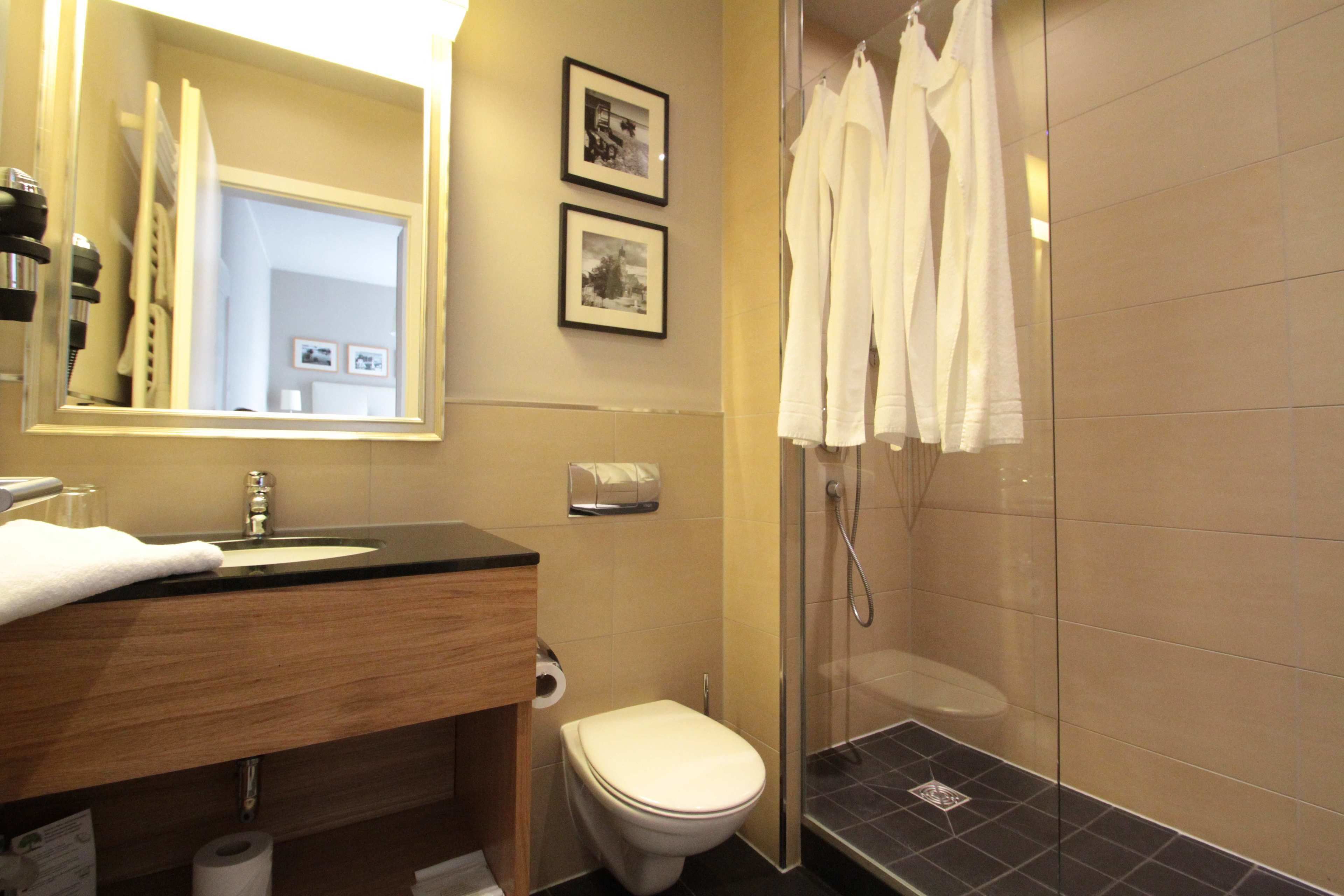 A bathroom with a sink, toilet, and shower. There are towels hanging on the wall and a mirror above the sink.