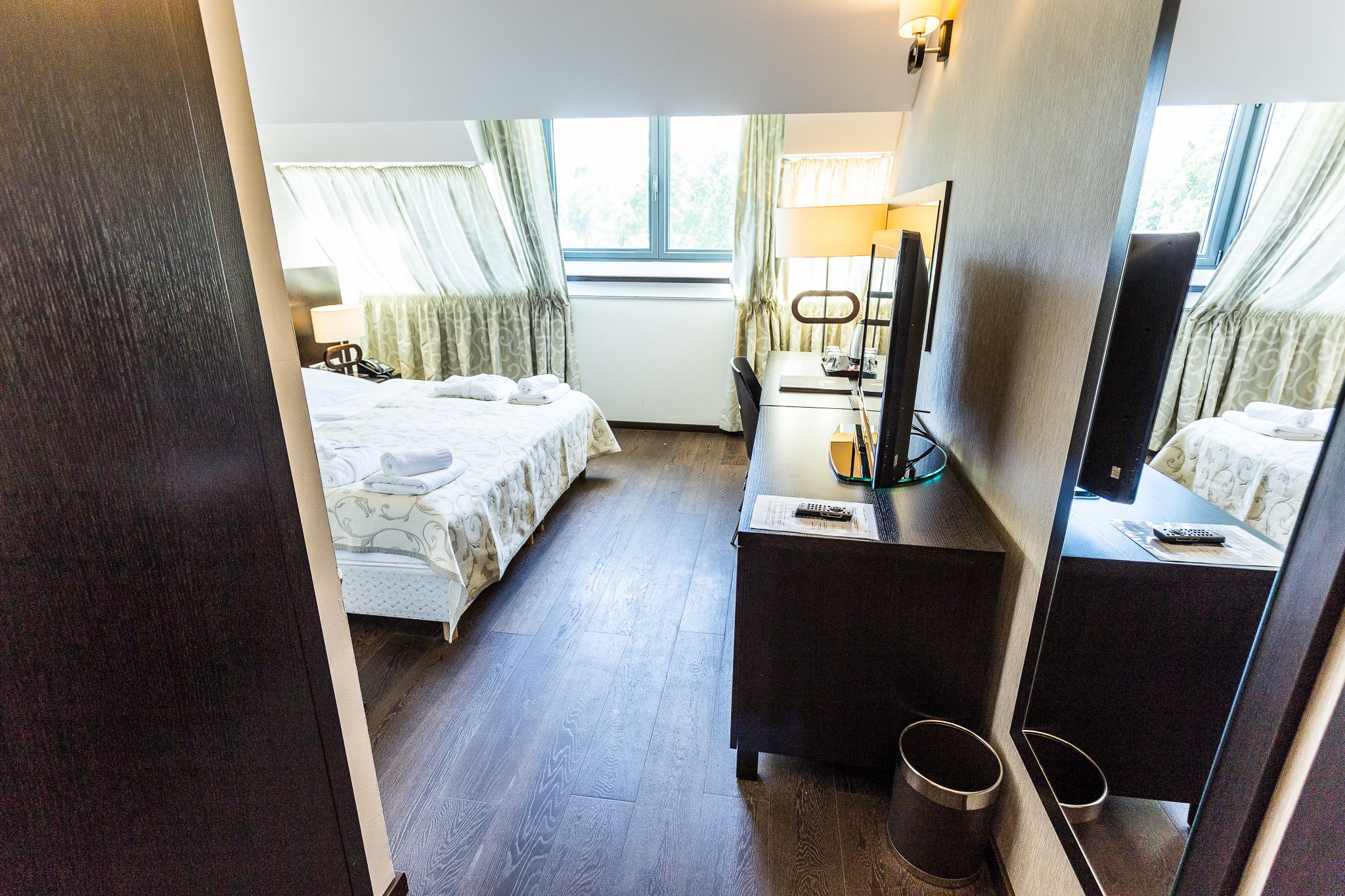 A hotel room with a bed, a desk, a mirror, and a window.