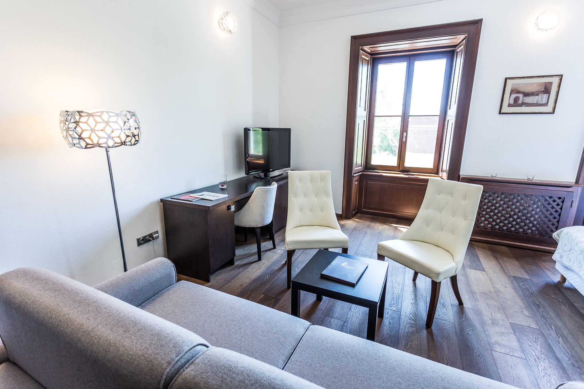 Ein Zimmer mit einer Couch, zwei Sesseln, einem kleinen Tisch, einem Schreibtisch mit Computer, einem Fernseher und einem Fenster mit Blick.