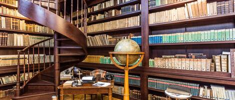 Una biblioteca con una escalera de caracol, estanterías de madera y un globo terráqueo sobre un atril.
