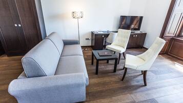 A modern living room with a grey sofa, two white armchairs, a small table, a floor lamp, and a TV.