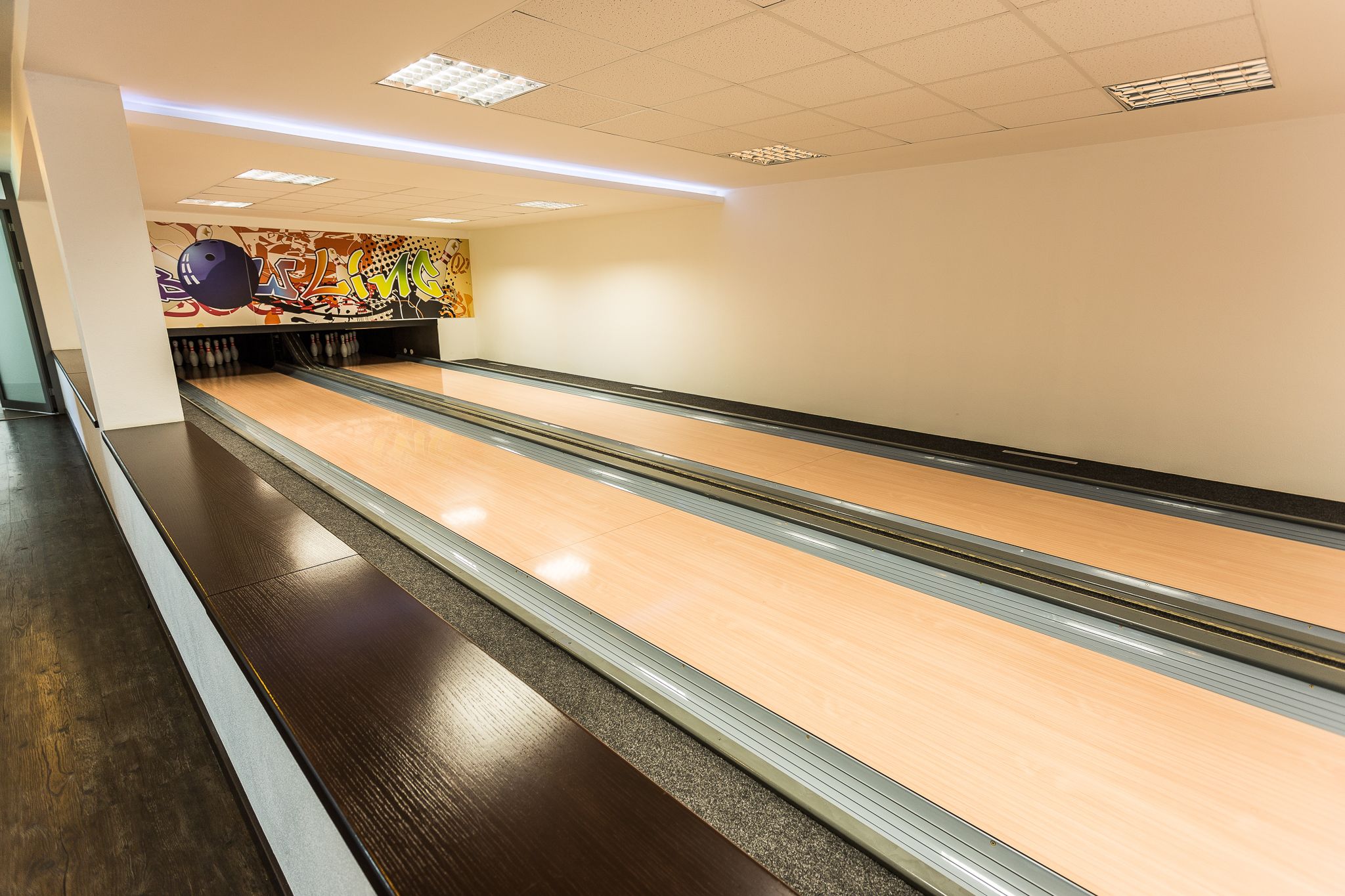 A bowling alley with multiple lanes, a colorful mural on the wall, and a clean, well-lit environment.