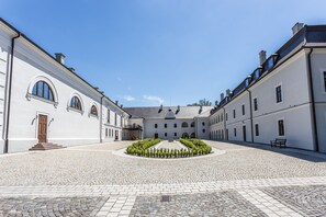A courtyard with cobblestone flooring, surrounded by white buildings with arched windows and a central garden. - Chateau Appony (Oponice)