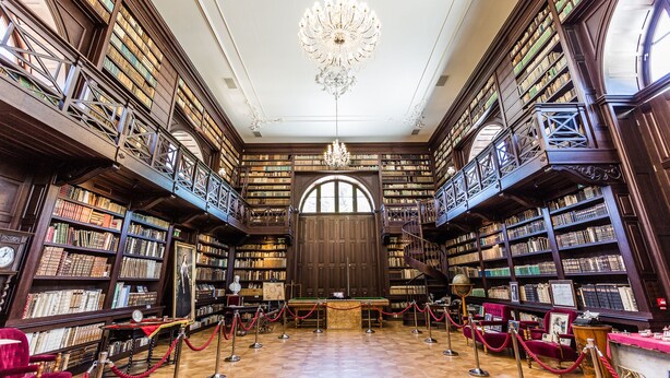 A grand library with high wooden bookshelves, a large arched doorway, and a central chandelier. - Chateau Appony (Oponice)