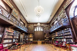 A grand library with high wooden bookshelves, a large arched doorway, and a central chandelier. - Chateau Appony (Oponice)