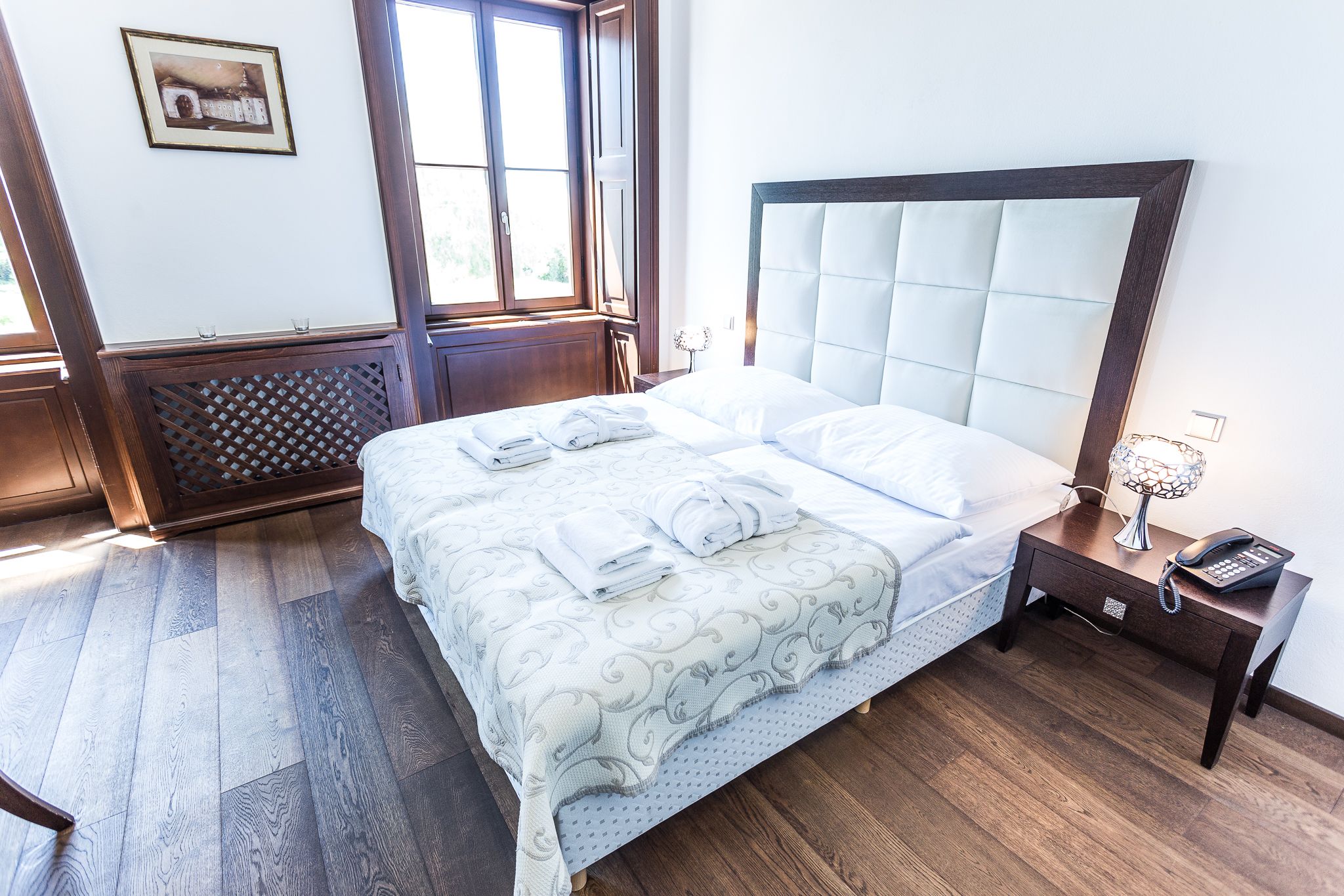 A neatly made bed with a patterned bedspread, a bedside lamp, and a phone on a wooden nightstand.