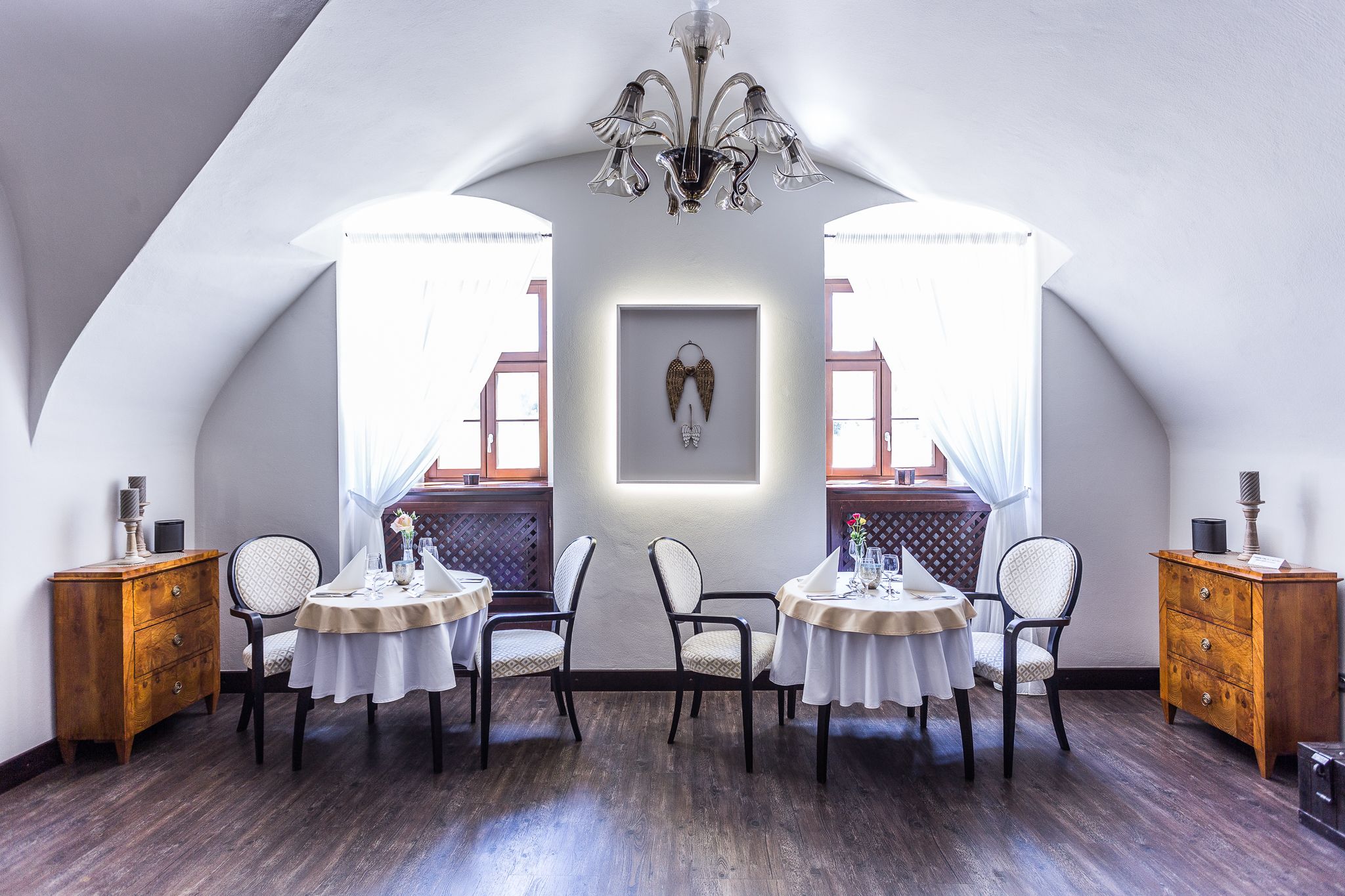 Un comedor con dos mesas redondas, sillas, una araña y armarios de madera.