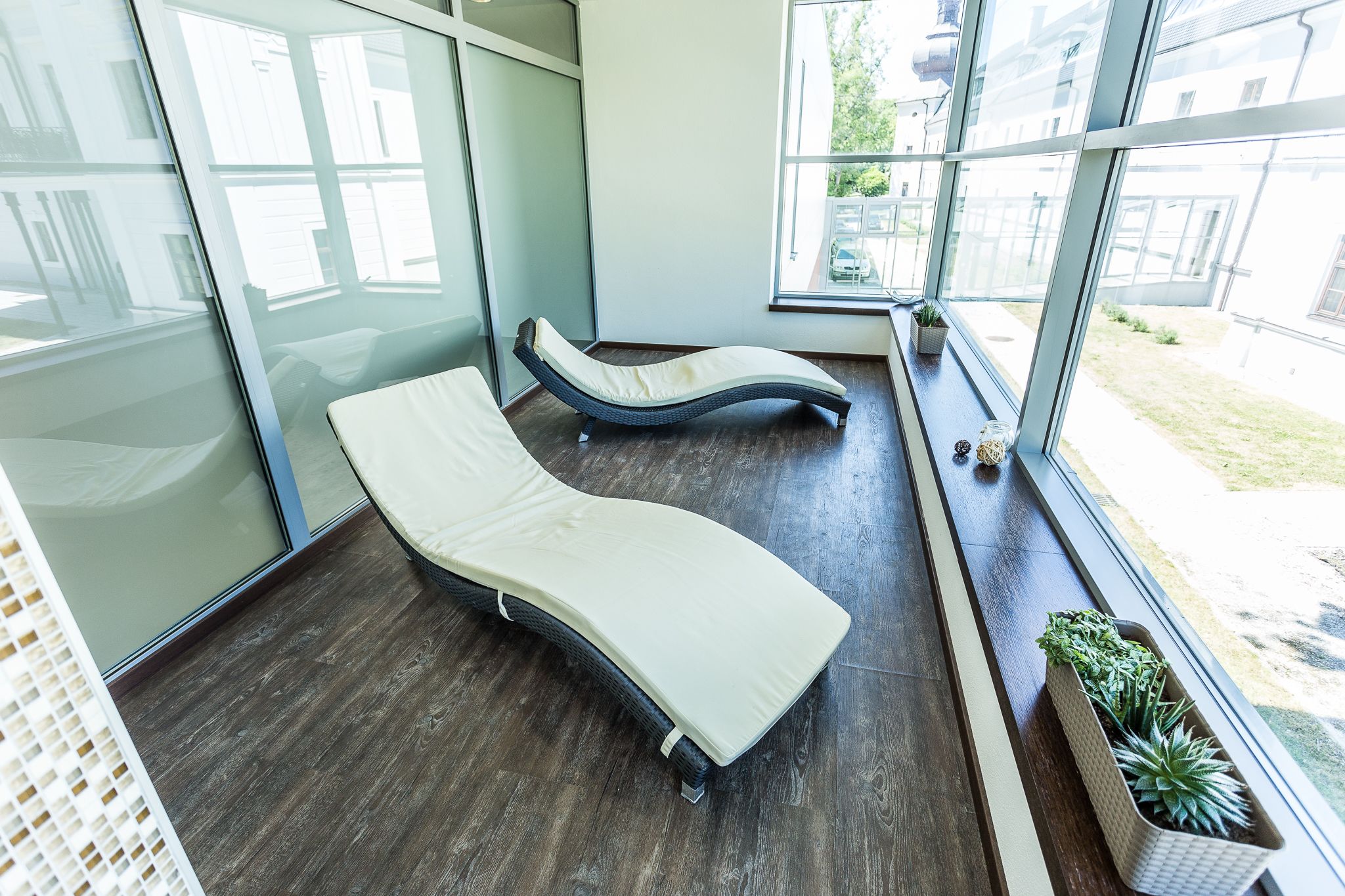 A modern room with two reclining massage beds, large windows, and potted plants.