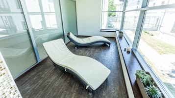 A modern room with two reclining massage beds, large windows, and potted plants.