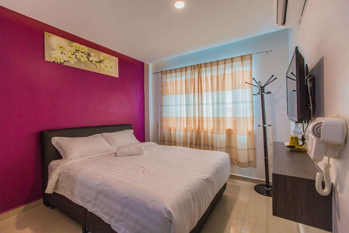 A hotel room with a bed, a television, a hairdryer, and a window with curtains.