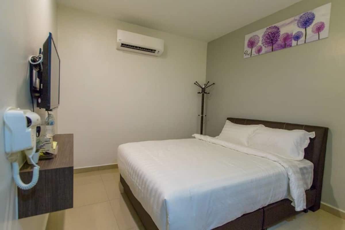 A hotel room with a bed, a desk with a telephone, an air conditioning unit, and a coat rack.