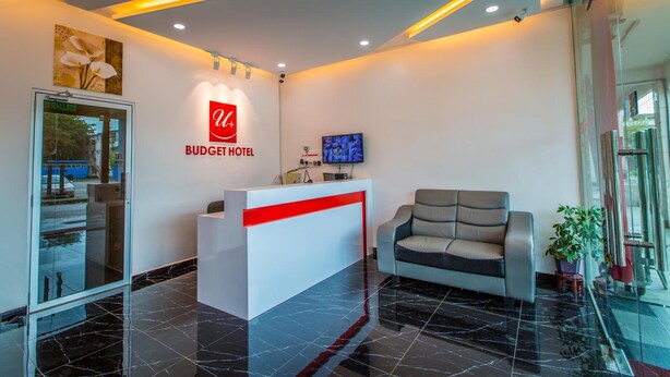 A reception area with a white reception desk, a red accent, a grey sofa, and a TV on the wall. - U Plus Budget Hotel (Bukit Mertajam)
