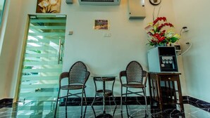 A room with a glass door leading to a balcony, two wicker chairs, a small table, an air conditioning unit, a water dispenser, and a flower vase. - U Plus Budget Hotel (Bukit Mertajam)
