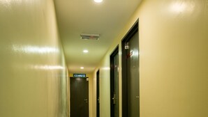 A long, narrow hallway with a tiled floor and cream-colored walls. There are doors on the right side, and a sign above one door reads "KELHARD." - U Plus Budget Hotel (Bukit Mertajam)