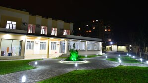 A building with multiple windows and air conditioning units, a paved walkway, and a circular garden with lights. - Planet Inn Hotel Baku (Baku)