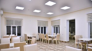 A spacious dining area with multiple tables and chairs, large windows with blinds, and a checkered floor pattern. - Planet Inn Hotel Baku (Baku)