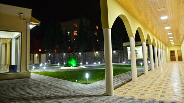 A covered walkway with columns, a green-lit fountain, and a building in the background. - Planet Inn Hotel Baku (Baku)