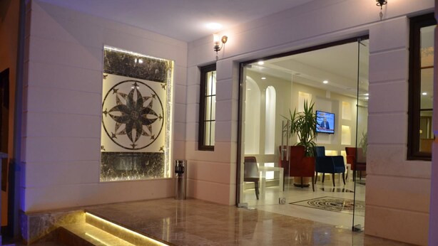A modern lobby with a marble floor, a large decorative wall piece, a staircase, and a seating area with chairs and a television. - Apameia Hotel (Mudanya)
