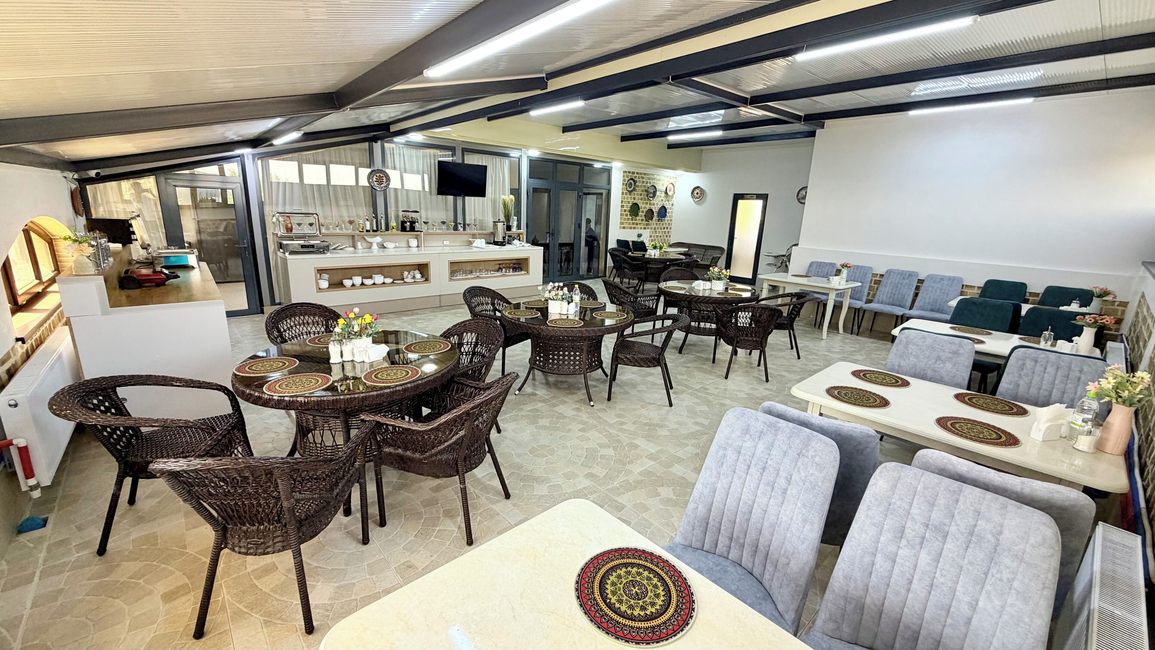A spacious dining area with wicker chairs and tables, a kitchen area with a bar, and a seating area with cushioned chairs.