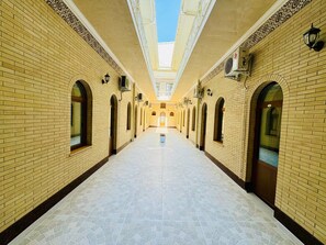 A long corridor with brick walls and arched windows, leading to a central open space with a skylight. - Samarkand Travel (Samarkand)