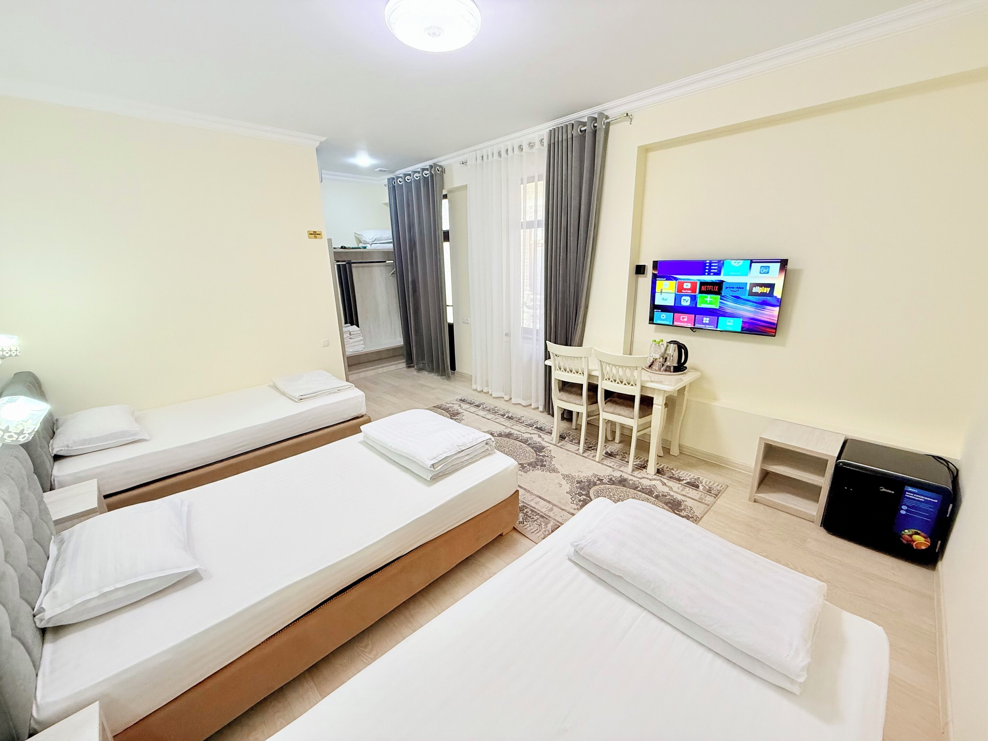 A hotel room with two beds, a desk, a TV, and a small kitchenette.