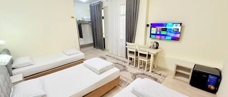 A hotel room with two beds, a desk, a TV, and a small kitchenette.