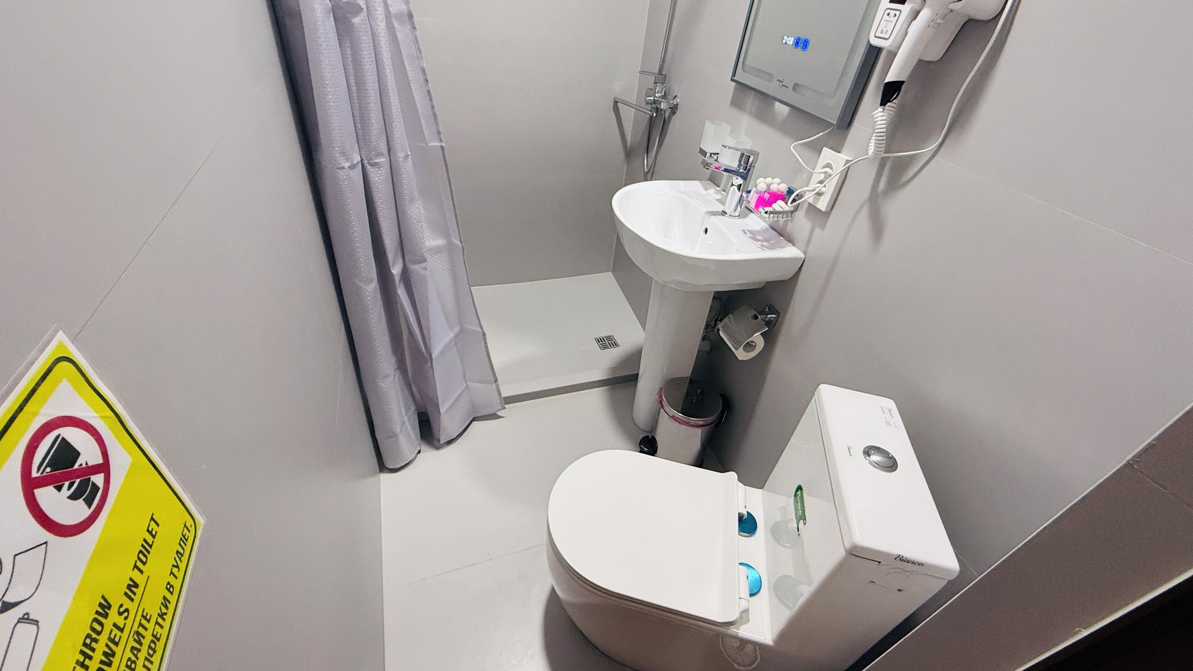 Pieni kylpyhuone, jossa on wc, pesuallas ja suihku. Seinällä on kyltti, jossa kerrotaan, ettei pyyhkeitä saa viedä wc:hen.