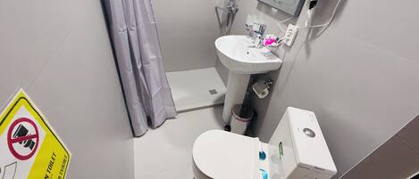A small bathroom with a toilet, sink, and shower. There is a sign on the wall indicating no towels in the toilet.