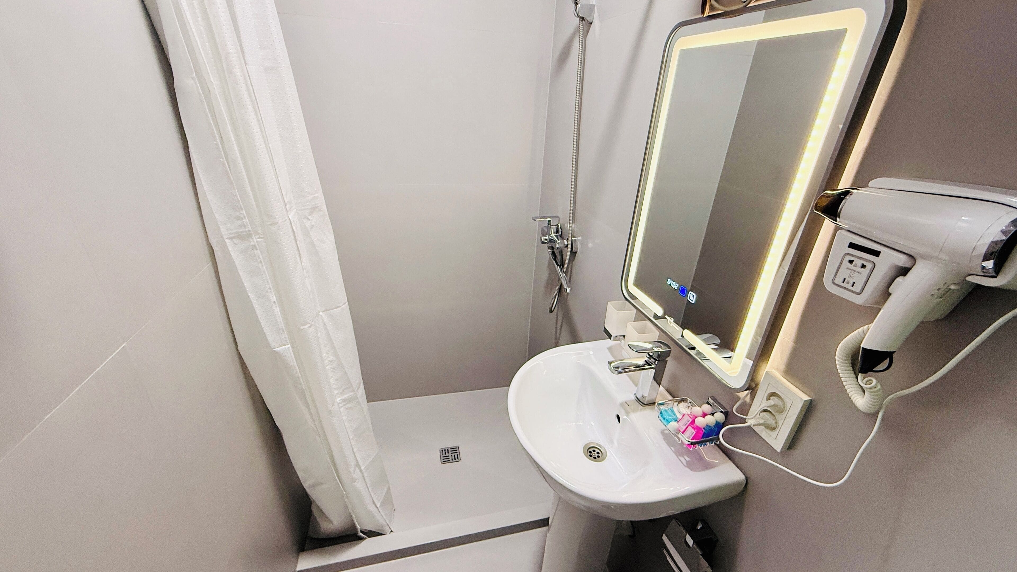 A bathroom with a shower, a sink, a mirror, and a hairdryer.