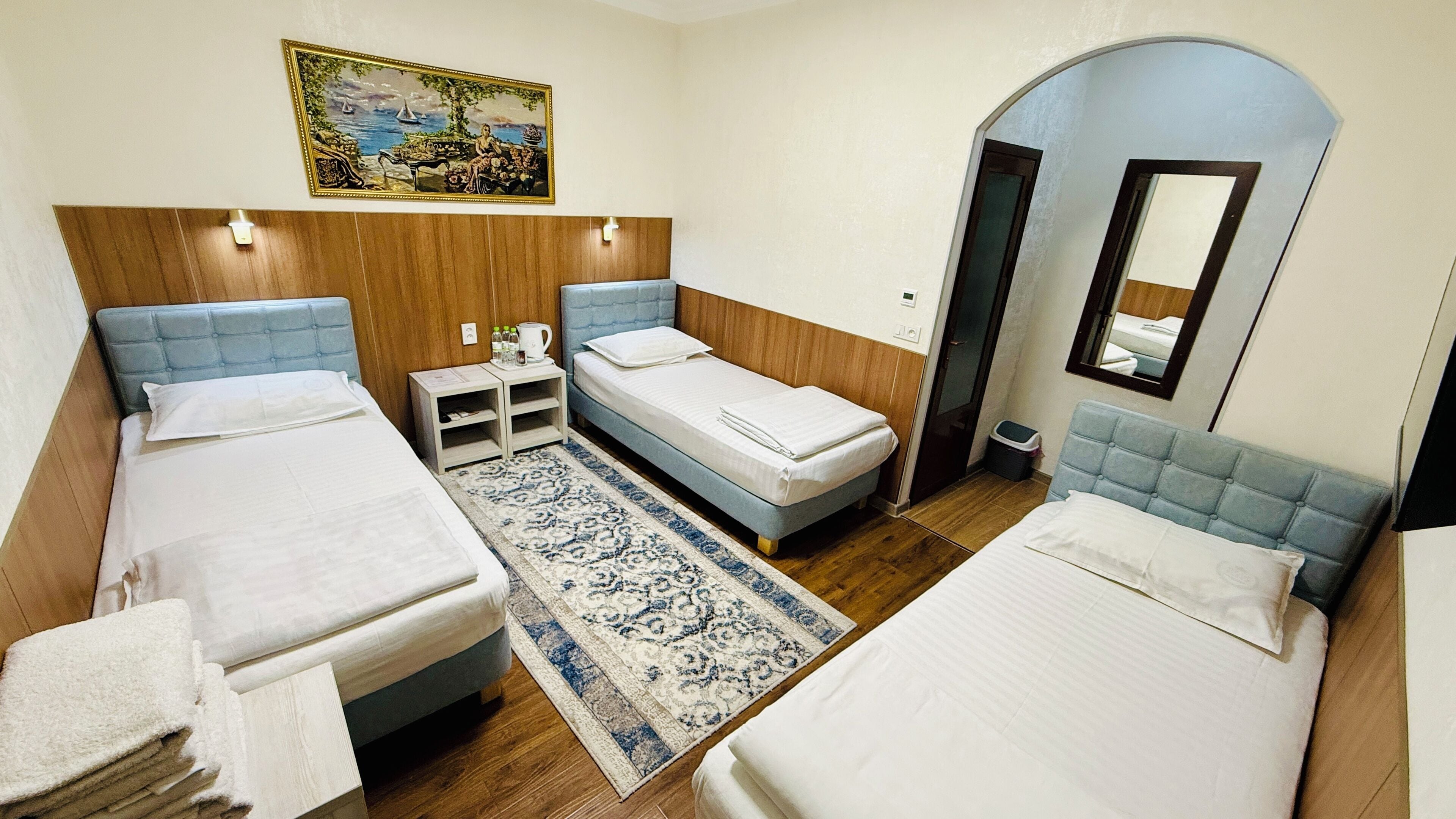 Ein Hotelzimmer mit zwei Betten, einem kleinen Tisch mit Wasserkocher, einem Teppich und einem Bild an der Wand.
